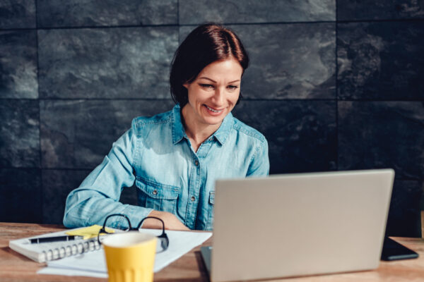 Vrouw lachend achter aan bureau met laptop. Templates inkoop.